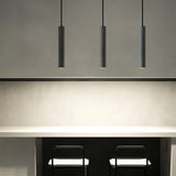 "Three gray cylindrical pendant lights hanging above a kitchen island counter with two black stools."