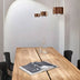 Three copper cylinder pendant lights hang above a wooden conference table with black chairs.