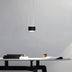 Black pendant light with white cord hanging above a desk with books and coffee cup.