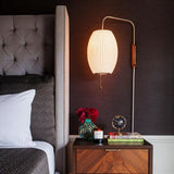 "A modern wall lamp with a luxurious silk shade illuminates a contemporary bedroom nightstand, creating a warm and elegant ambiance."