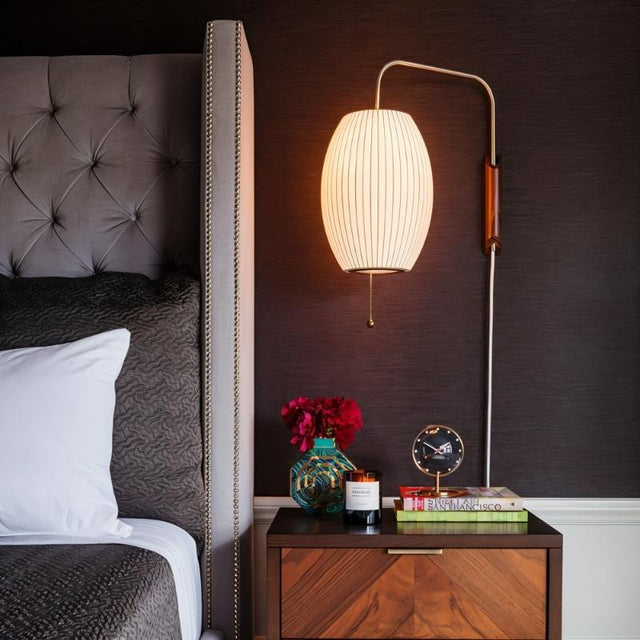 "A modern wall lamp with a luxurious silk shade illuminates a contemporary bedroom nightstand, creating a warm and elegant ambiance."