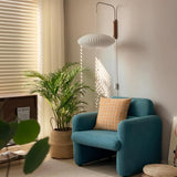 "A modern wall lamp with a silk shade illuminates a living room corner featuring a vibrant houseplant and a comfortable armchair."