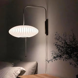 "A modern wall lamp with a luxurious silk shade illuminates a contemporary bedroom, casting a soft, warm glow."