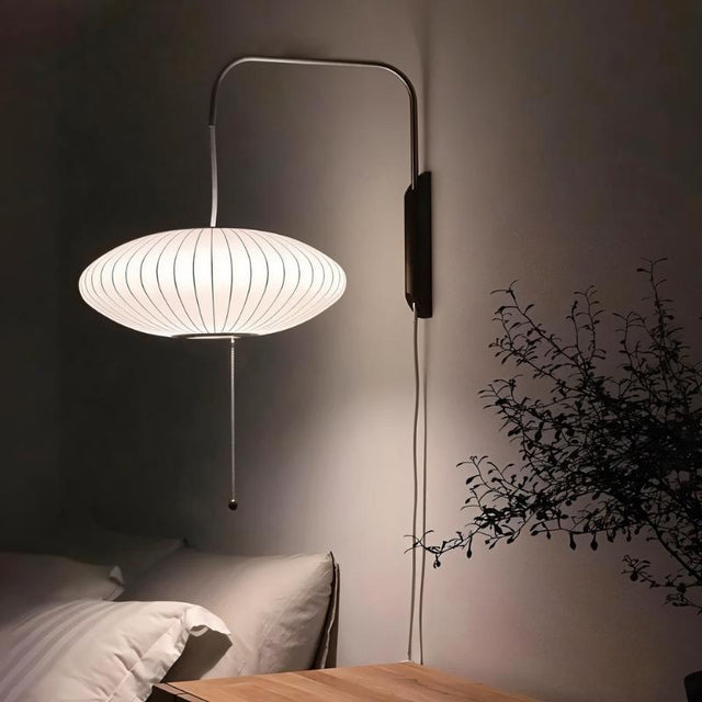 "A modern wall lamp with a luxurious silk shade illuminates a contemporary bedroom, casting a soft, warm glow."