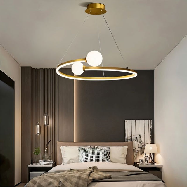 "A gold circular chandelier with two white spherical diffusers, hanging above a bed in a modern bedroom."