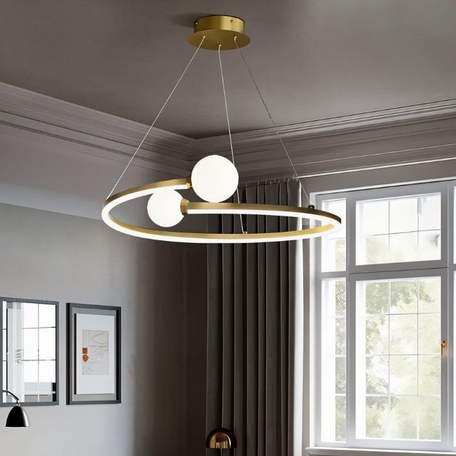 "A gold circular chandelier with two white spherical diffusers, hanging in a room with windows and artwork."