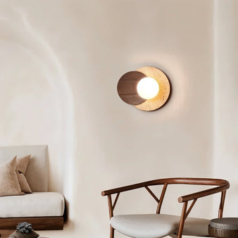 "A wabi-sabi wall lamp featuring travertine and wood, mounted on a light-colored wall, emitting a soft, ambient glow in a minimalist space."