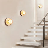 "Three wabi-sabi wall lamps with travertine and wood elements, arranged on a wall alongside a modern staircase, providing a soft, ambient glow."