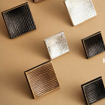 "Studio shot of square brass knobs with a ridged, textured surface on a neutral background."