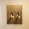 Double gang version of The Brass Toggle Switch (1 to 5 Gang) - Open Box featuring two knurled toggles on a matte brass faceplate for upscale lighting control.