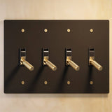 Four-gang The Brass Toggle Switch (1 to 5 Gang) - Open Box in black with gold toggles, perfect for high-end lighting installations.