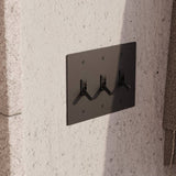 Triple gang The Brass Toggle Switch (1 to 5 Gang) - Open Box in matte black finish, mounted on textured concrete wall for modern industrial decor.