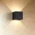 White cubic wall sconce with uplight and downlight casting warm illumination on modern architectural exterior at dusk.