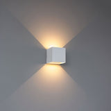"Close-up view of the Tine Wall Lamp on a gray wall, casting dual upward and downward light beams, crafted from gypsum and aluminum with a sleek, minimalist design."