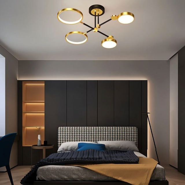 "A modern ceiling light with four circular lights and black metal accents installed in a bedroom with a patterned headboard and dark walls."