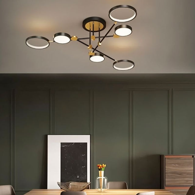 "A modern ceiling light with six circular lights and black metal accents installed above a dining table in a room with dark green walls."