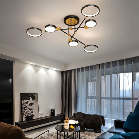 "A modern ceiling light with six circular lights and black metal accents installed in a living room with a dark couch and large windows."