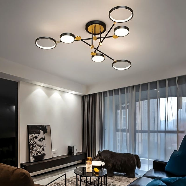 "A modern ceiling light with six circular lights and black metal accents installed in a living room with a dark couch and large windows."