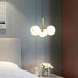 "A modern pendant light with three opal glass globes, in gold, hanging above a nightstand with flowers and a teddy bear."