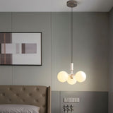"A modern pendant light with three opal glass globes, in white and gold, hanging in a bedroom with a tufted headboard and artwork."