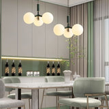 "Two modern pendant lights with three opal glass globes each, in green, hanging over a dining table with upholstered chairs."