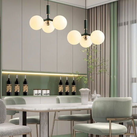 "Two modern pendant lights with three opal glass globes each, in green, hanging over a dining table with upholstered chairs."