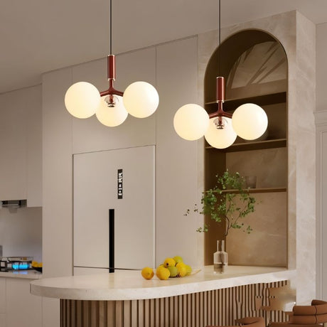 "Two modern pendant lights with three opal glass globes each, hanging over a kitchen island with a curved countertop."