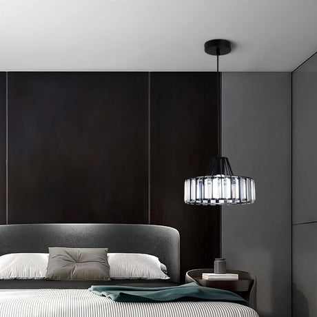 "A modern crystal pendant light with a black frame, hanging above a bed with pillows and a nightstand."