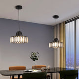 "Two modern crystal pendant lights with black frames, hanging above a dining table with chairs and a plant."