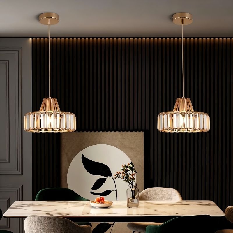  "Two modern crystal pendant lights with gold frames, hanging above a dining table with a marble top and artwork."