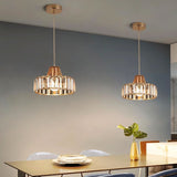 "Two modern crystal pendant lights with gold frames, hanging above a dining table with a plant and place settings."