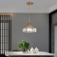 "A modern crystal pendant light with a gold frame, hanging above a dining table with a plant and white vases."