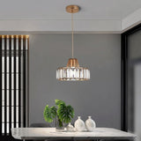 "A modern crystal pendant light with a gold frame, hanging above a dining table with a plant and white vases."
