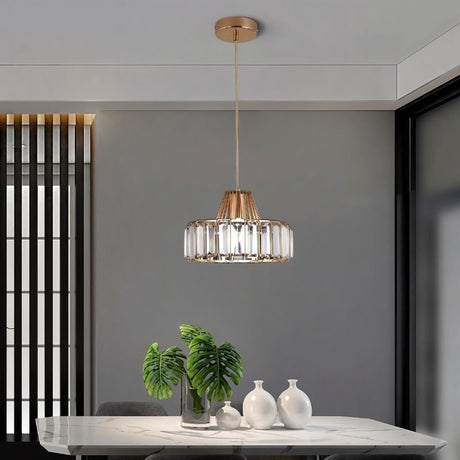 "A modern crystal pendant light with a gold frame, hanging above a dining table with a plant and white vases."