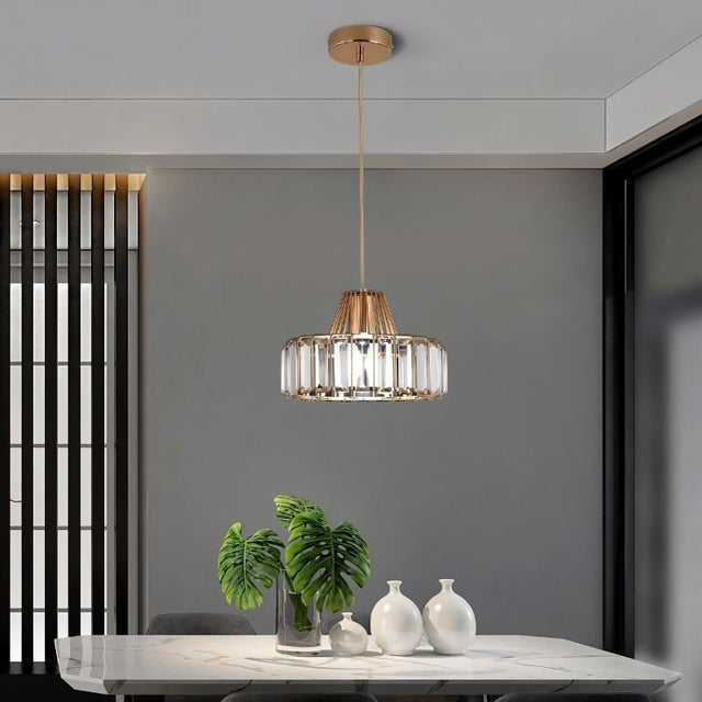 "A modern crystal pendant light with a gold frame, hanging above a dining table with a plant and white vases."
