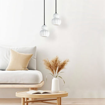 "Two modern pendant lights with white ceramic shades hang in a minimalist living room with a neutral palette."