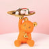 Orange bear figurine with gold accents holding a brass tray filled with decorative items on pink background.