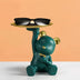 Teal bear figurine with gold accents holding a brass tray supporting black sunglasses against a peach and white background.
