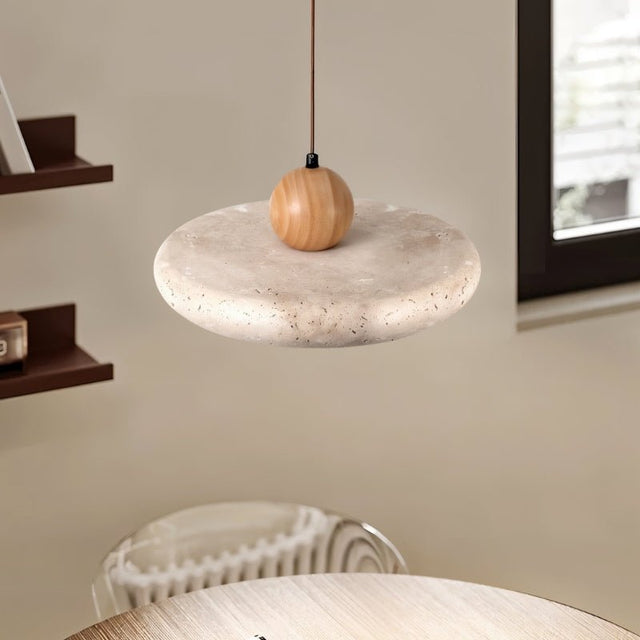 "Close-up detail of a modern pendant light with a circular travertine shade and a wooden sphere, showcasing the texture and materials."