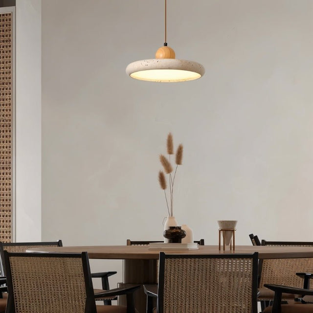 "Modern pendant light with a circular travertine shade and wooden sphere, hanging over a large dining table with wicker chairs."