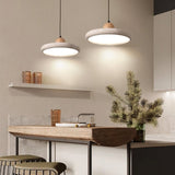 "Pair of modern pendant lights with circular travertine shades and wooden spheres, hanging over a kitchen island with stools and decorative items."