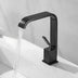 Black modern bathroom sink faucet with curved spout flowing water, mounted on white countertop.