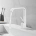 White square modern bathroom faucet with high arc spout flowing water over white sink basin.
