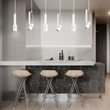 "White pendant lights with cylindrical shades, both straight and oblique, illuminating a modern kitchen island with stools."