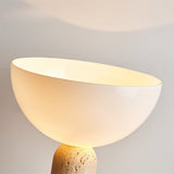 "Close-up of a glossy glass dome shade emitting a warm glow, supported by a textured travertine base"