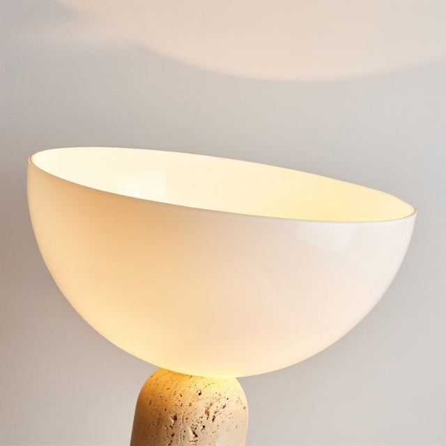 "Close-up of a glossy glass dome shade emitting a warm glow, supported by a textured travertine base"