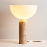 "Elegant table lamp with a travertine cylindrical base and a glowing glass dome shade, creating warm ambient lighting"