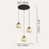 Three-light pendant chandelier with black metal canopy and golden crystal ball shades, shown against neutral background.