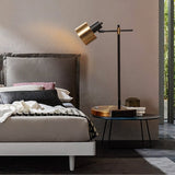 "Iron and brass table lamp with rotatable head, placed on a bedside table in a modern bedroom with clean lines"