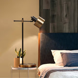 "Iron and brass table lamp with a rotatable head, placed next to a bed on a modern nightstand, adding a sleek touch to the bedroom"
